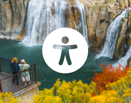 An illustrated accessibility icon over an image of two people standing at a viewpoint at Shoshone Falls with fall foliage in the foreground.