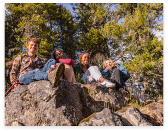 A group of four people sitting large rocks backed by tall trees at Middle Elk Creek Falls.