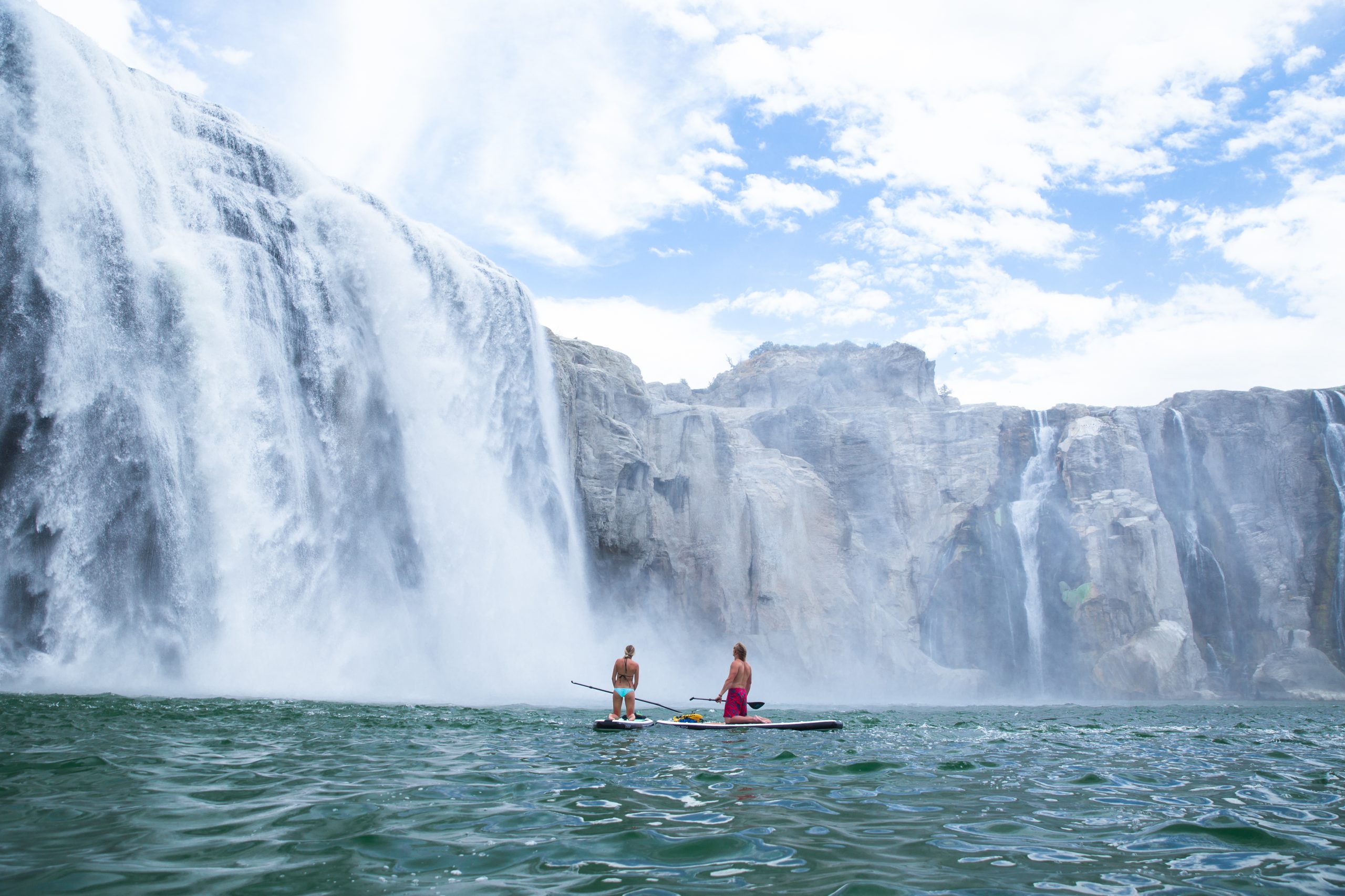 Two people stand up paddleboarding in front of Shoshone Falls.