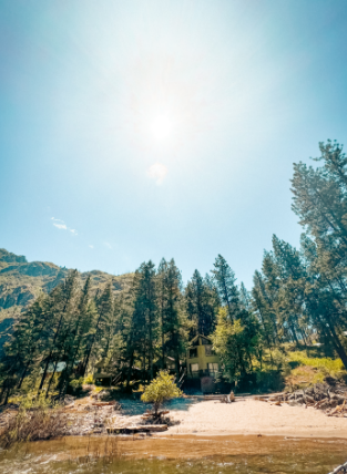 A body of water before a sandy beach and a forest of trees and a small house in the background.